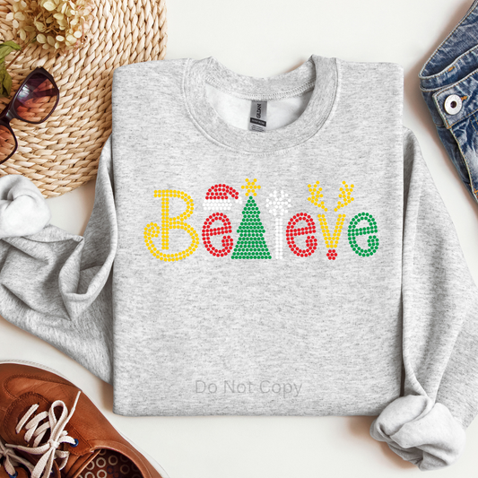 Gray sweatshirt with 'Believe' in colorful letters on a white surface with accessories.